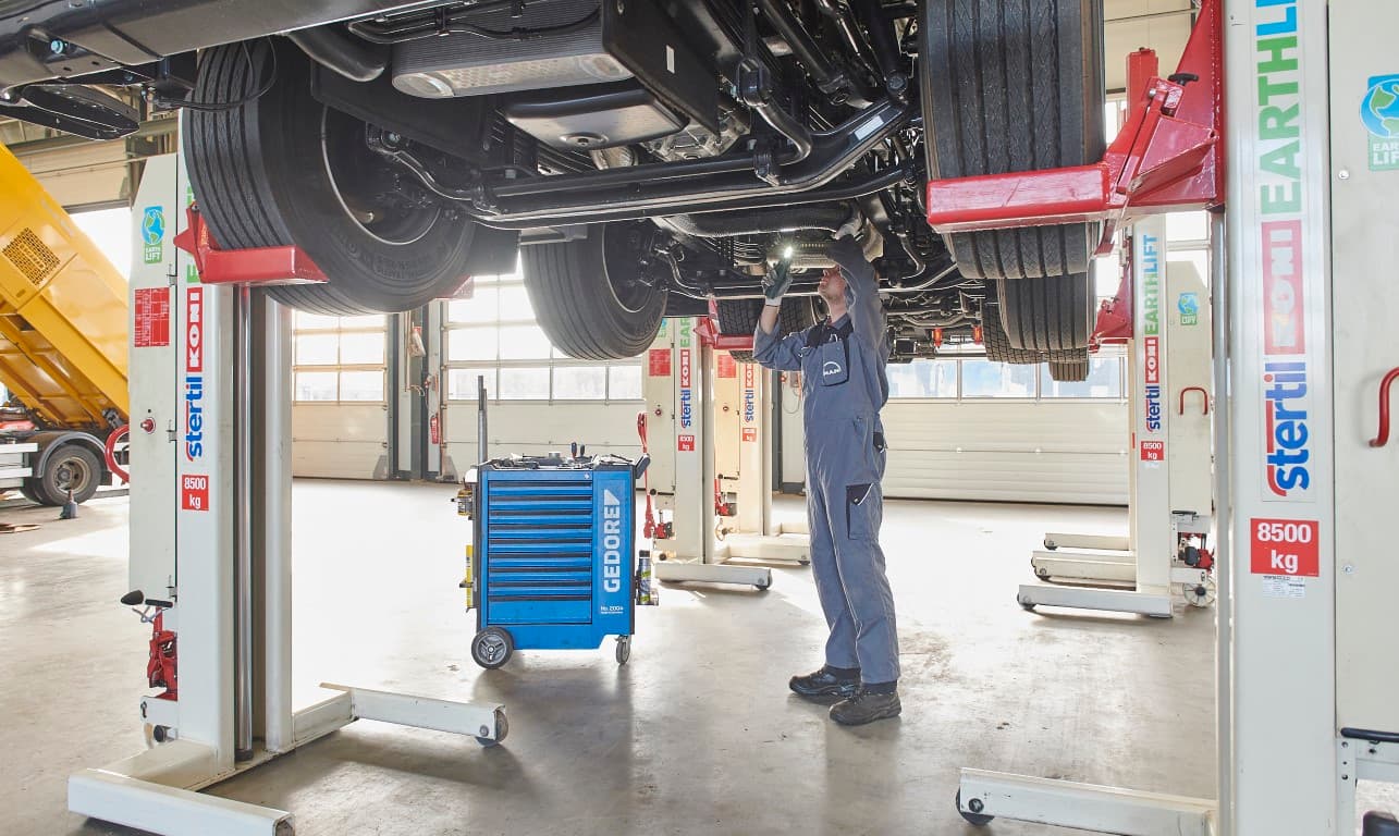 Mechanic standing upright and working underneath a truck which is lifted with mobile column vehicle lifts from Stertil-Koni